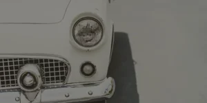 Front view of a white classic car with chrome bumper parked on a light gray surface.
