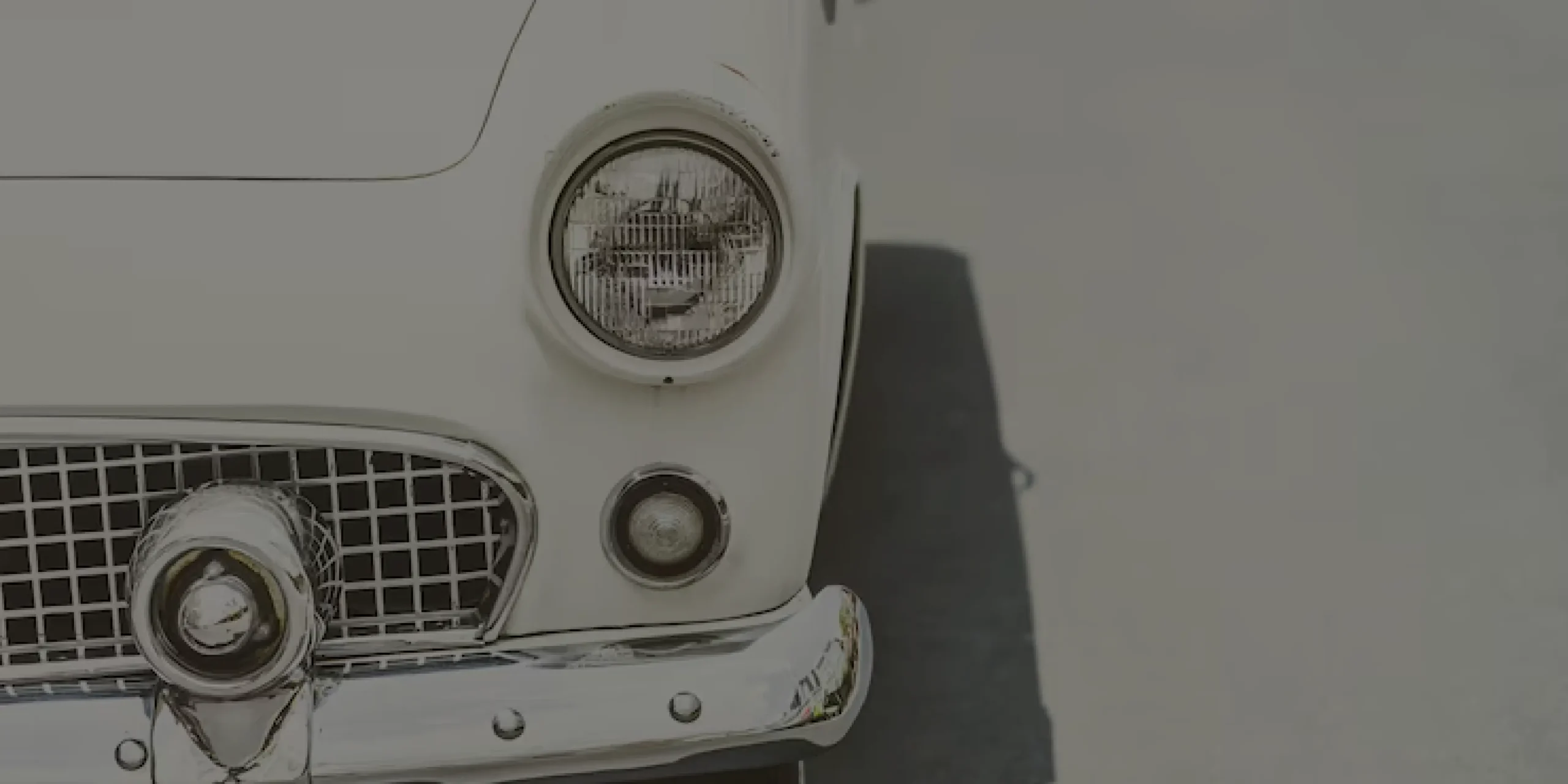 Front view of a white classic car with chrome bumper parked on a light gray surface.