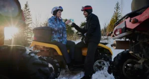 Two riders enjoying a break on all-terrain vehicles in a snowy forest, symbolizing the fun and risks covered by ATV insurance.
