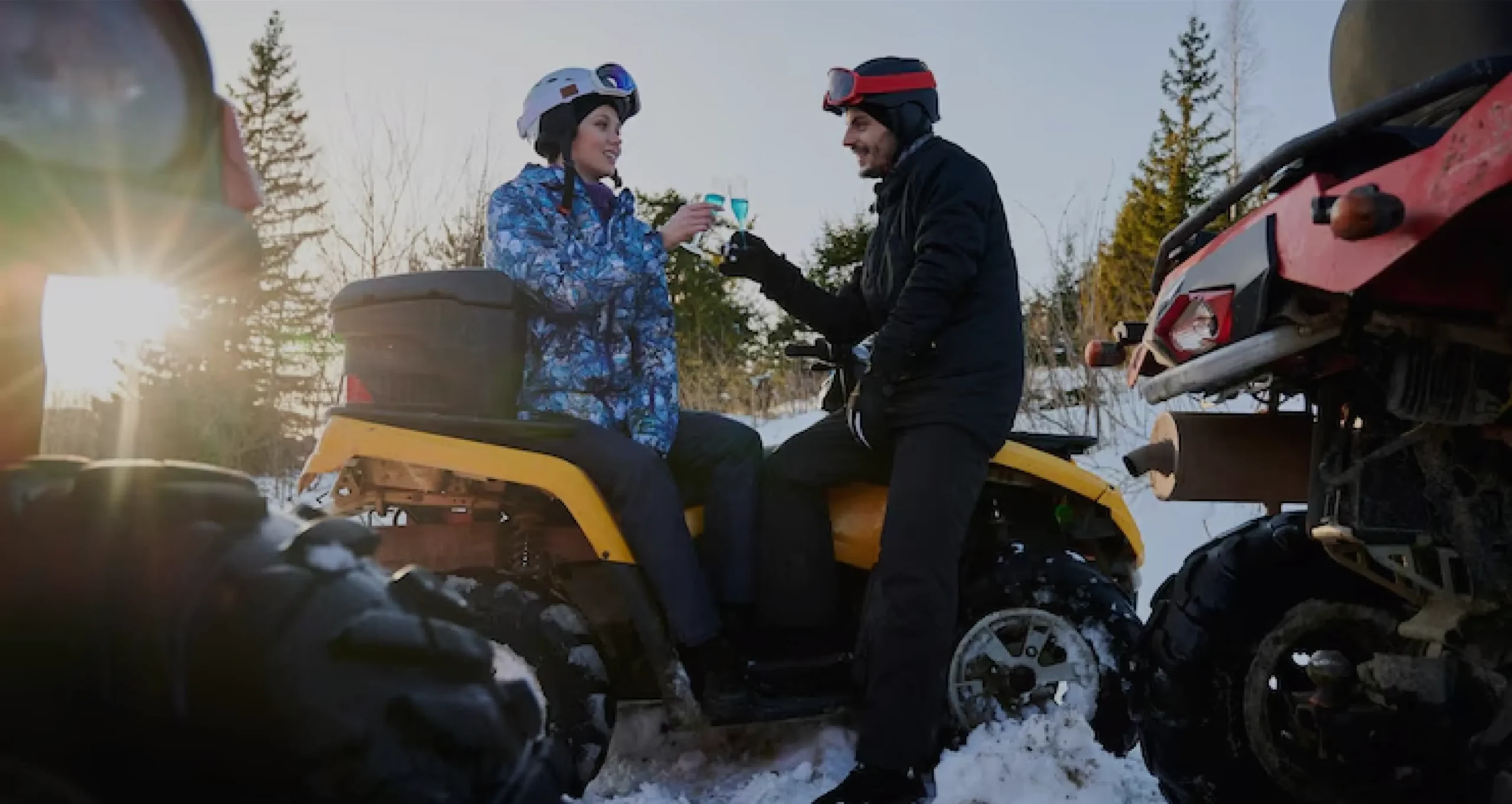 Two riders enjoying a break on all-terrain vehicles in a snowy forest, symbolizing the fun and risks covered by ATV insurance.